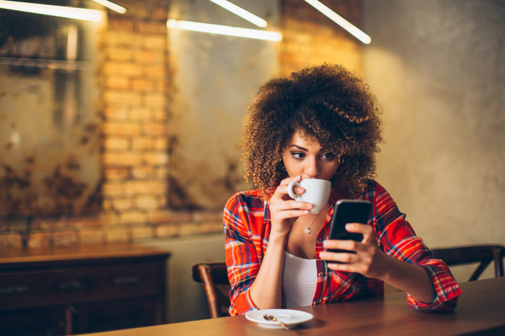 Young woman at cafe drinking coffee and using mobile phone for V1C